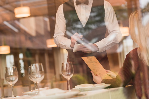 Hotelservice: Ein Kellner nimmt die Bestellung einer Frau auf. Es ist ein sehr schönes Lokal. Das Bild strahlt Wärme.